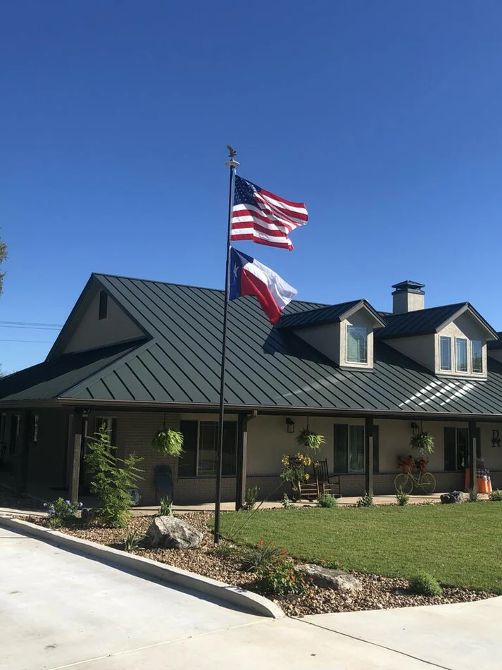 A Phoenix flagpole flying the American and Texas flags in front of a home