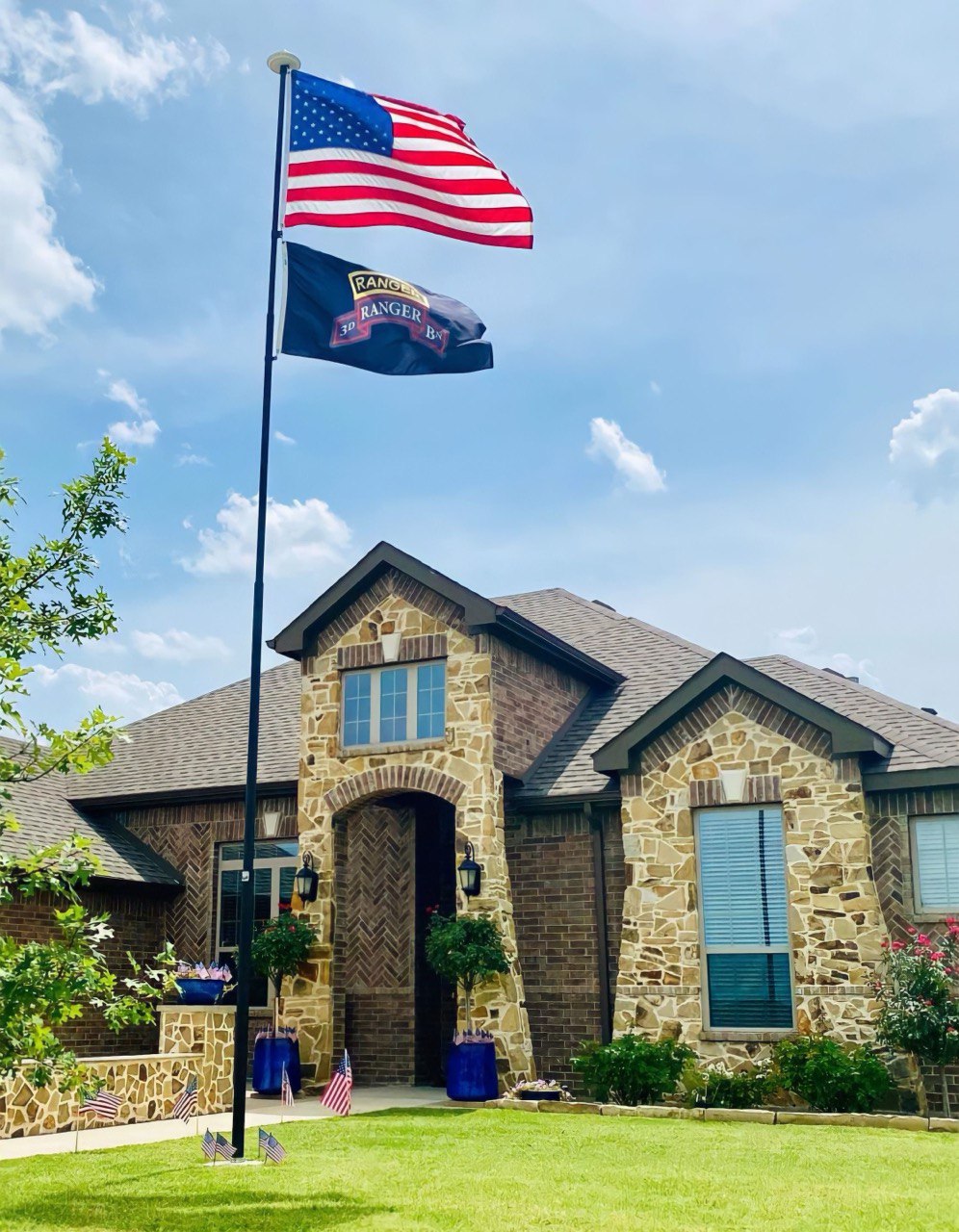 A Phoenix flagpole flying the American flag and a second flag in front of a stone home